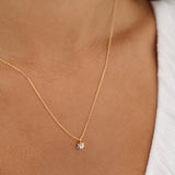 Gold necklace with a small pendant on a person wearing a white top.