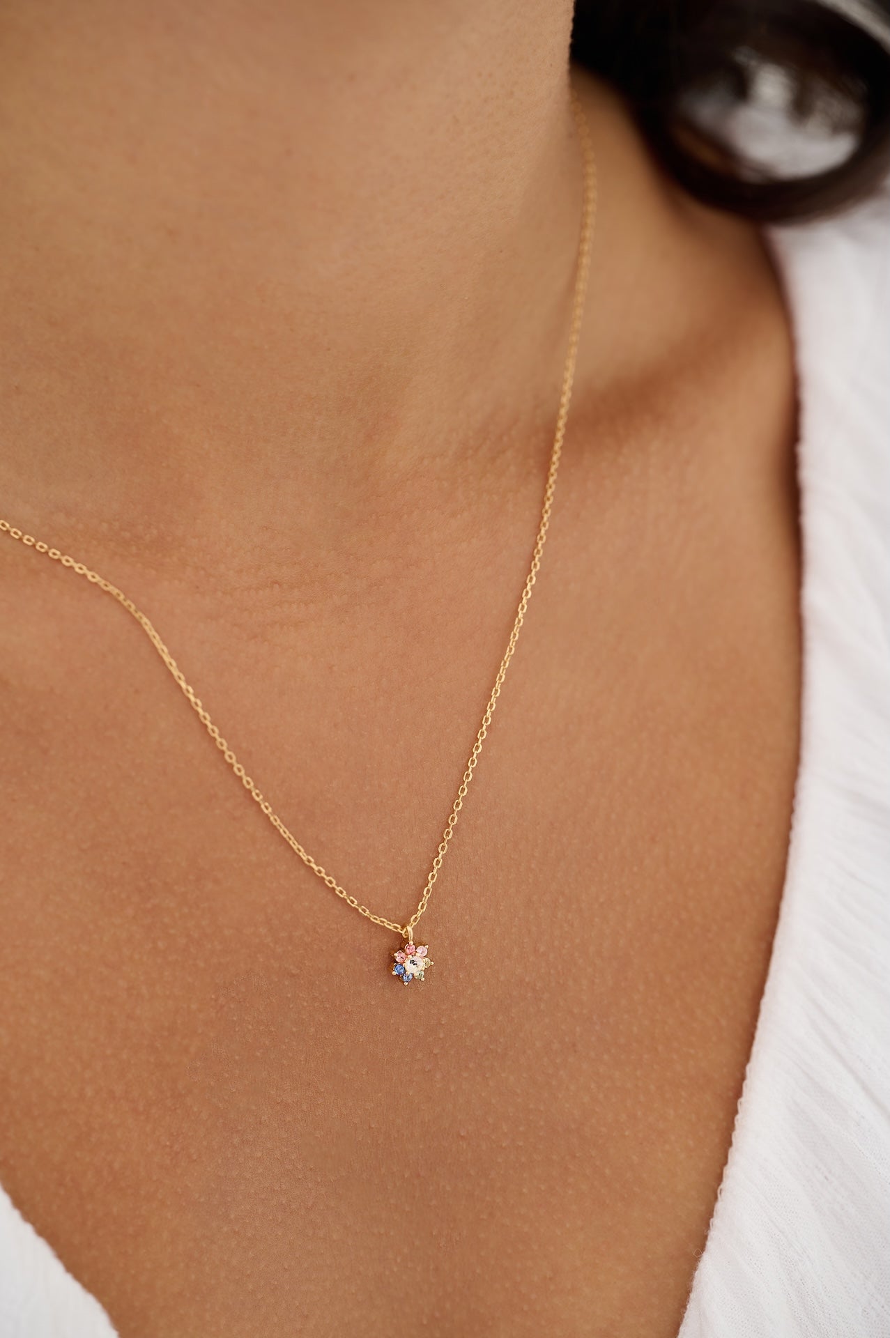 Gold necklace with a small pendant on a person wearing a white top.