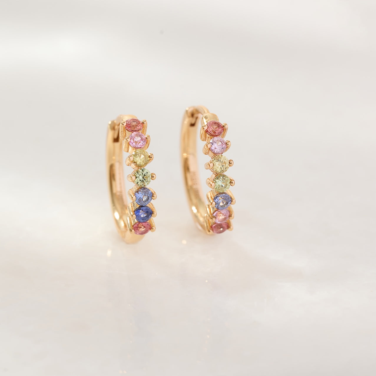 Gold hoop earrings with colorful gemstones on a light gray background