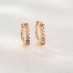 Gold hoop earrings with colorful gemstones on a light gray background