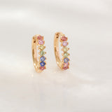 Gold hoop earrings with colorful gemstones on a light gray background