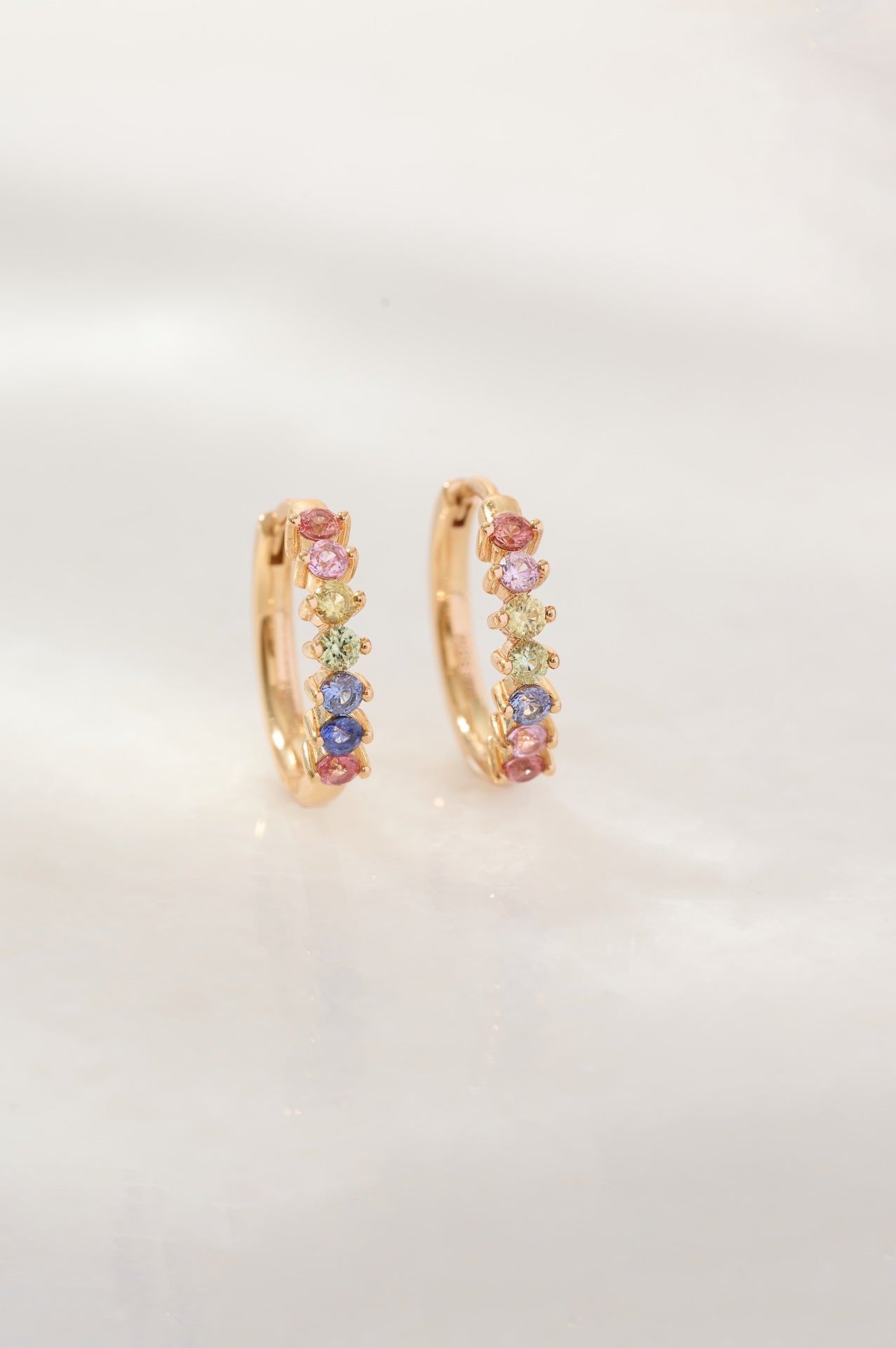 Gold hoop earrings with colorful gemstones on a light gray background