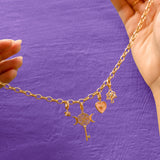 Gold necklace with charms held against a purple background