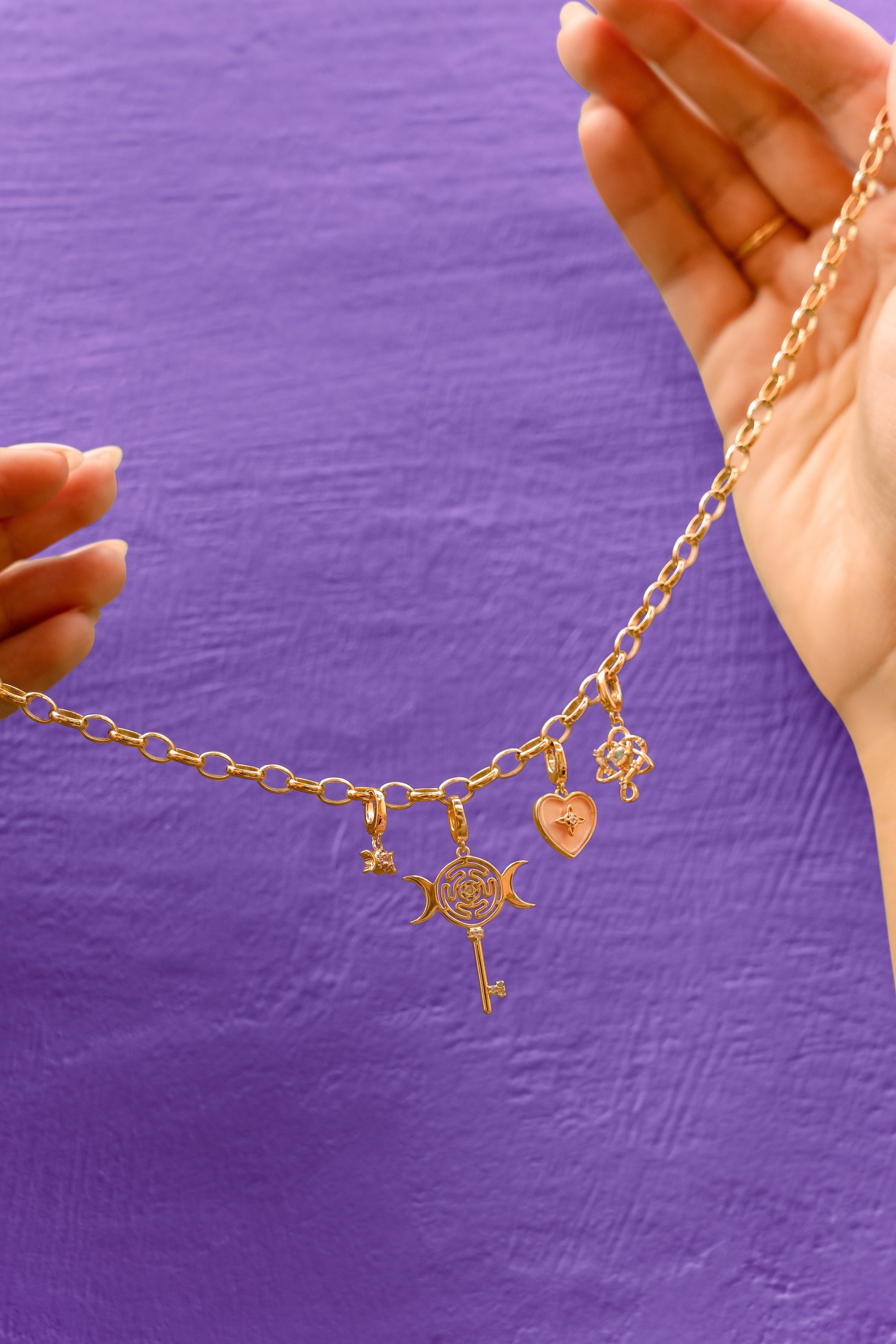 Gold necklace with charms held against a purple background