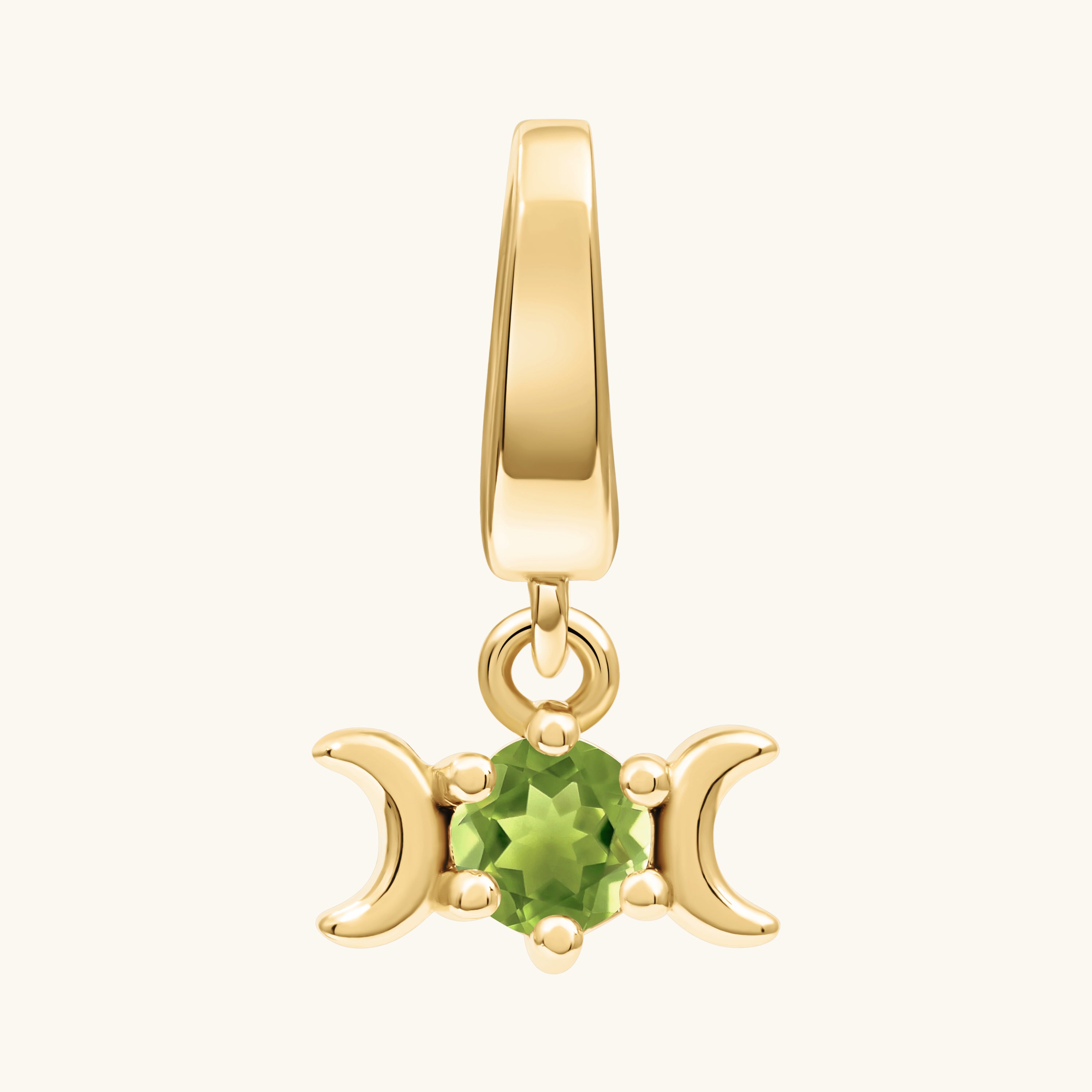 A gold pendant charm featuring a central green peridot gemstone flanked by two crescent moons, shown on a light cream background.