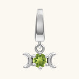 A sterling silver triple moon charm featuring a central faceted green peridot gemstone, set against a plain off-white background.