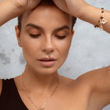 A close-up lifestyle shot of a woman wearing a delicate gold chain necklace with a small black pendant and a matching gold bracelet, set against a textured gray background.