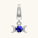 A silver-toned triple moon charm pendant featuring a faceted deep blue gemstone in the center, set against a plain off-white background.
