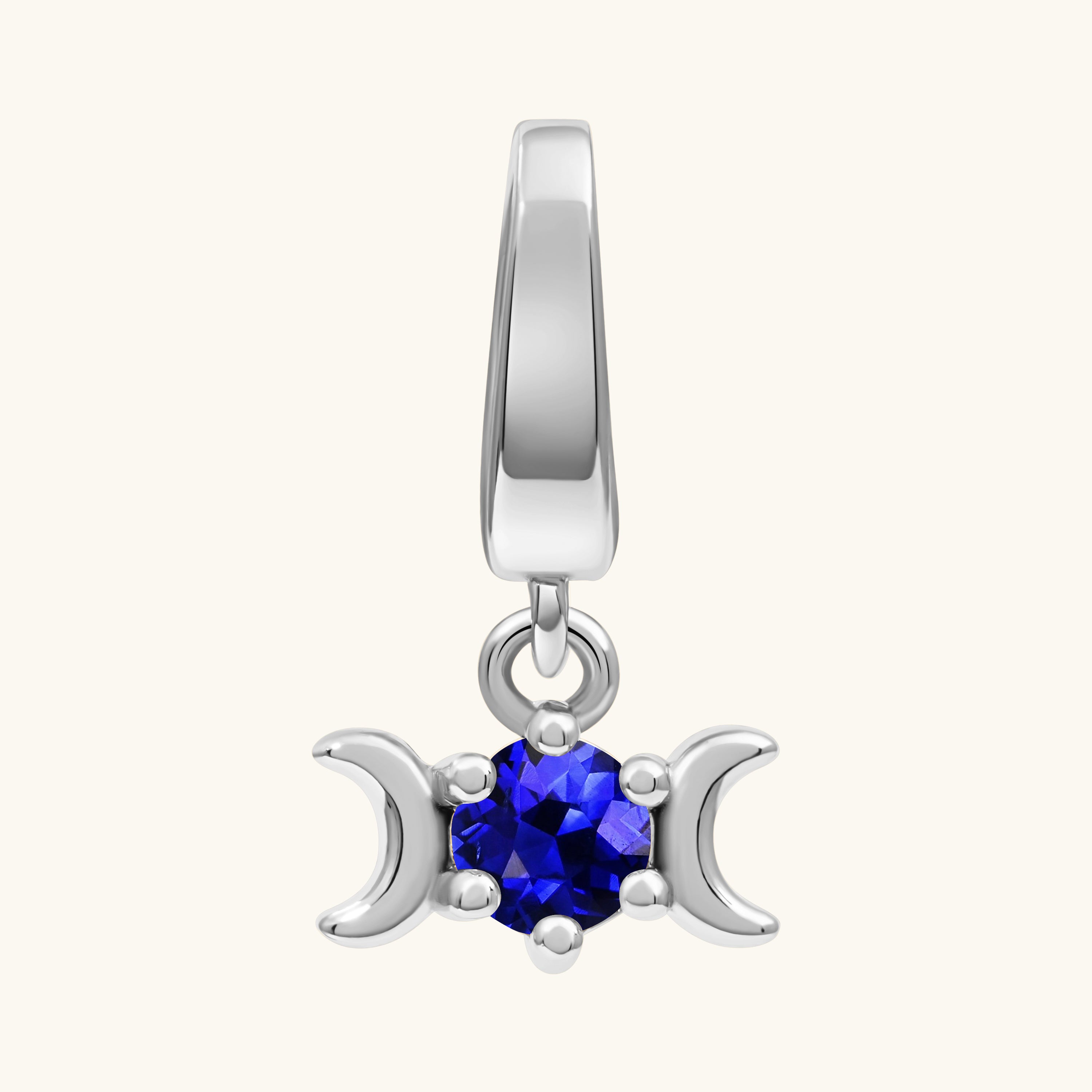 A silver-toned triple moon charm pendant featuring a faceted deep blue gemstone in the center, set against a plain off-white background.