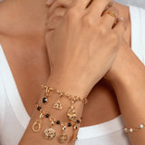 A close-up of a model's wrist wearing a layered stack of gold charms paired with a white ribbed top.