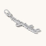 The word magickal is written in elegant cursive script and studded with white topaz stones. It is set in a silver charm pendant against an light cream background. 