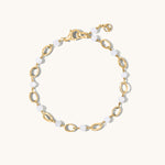 A gold-tone chain bracelet with alternating polished oval links and smooth round white beads, displayed on a clean off-white background.