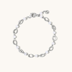 A silver-toned link bracelet featuring alternating polished oval links and smooth white bead links, displayed on a clean off-white background.