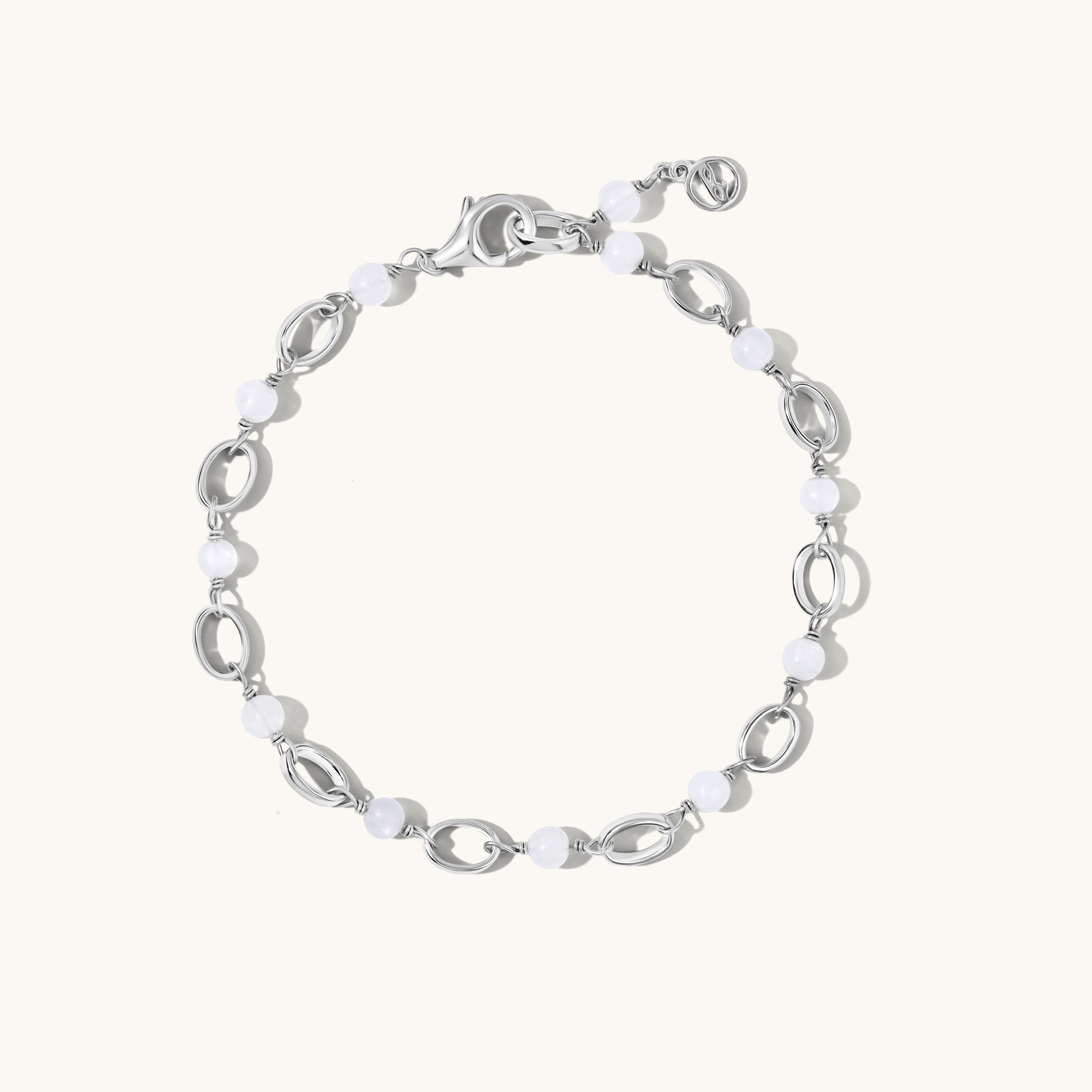 A silver-toned link bracelet featuring alternating polished oval links and smooth white bead links, displayed on a clean off-white background.