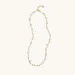 A delicate gold and white beaded necklace with alternating gold oval links and small white beads, displayed on a clean off-white background.