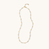 A delicate gold and white beaded necklace with alternating gold oval links and small white beads, displayed on a clean off-white background.