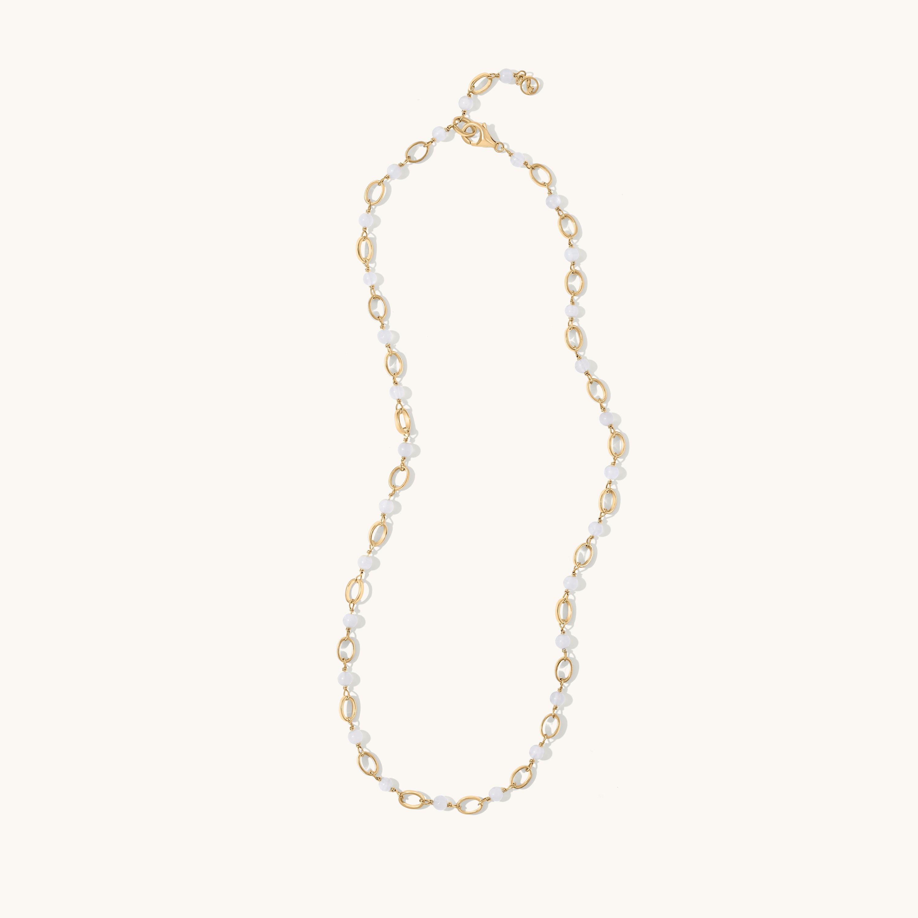 A delicate gold and white beaded necklace with alternating gold oval links and small white beads, displayed on a clean off-white background.