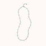 A delicate silver chain necklace with alternating small oval links and tiny clear faceted beads, displayed on a solid off-white background.