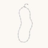 A delicate silver chain necklace with alternating small oval links and tiny clear faceted beads, displayed on a solid off-white background.