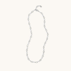 A delicate silver chain necklace with alternating small oval links and tiny clear faceted beads, displayed on a solid off-white background.