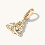 Stone studded Gold Triquetra symbol charm lying on a light cream background with shadow