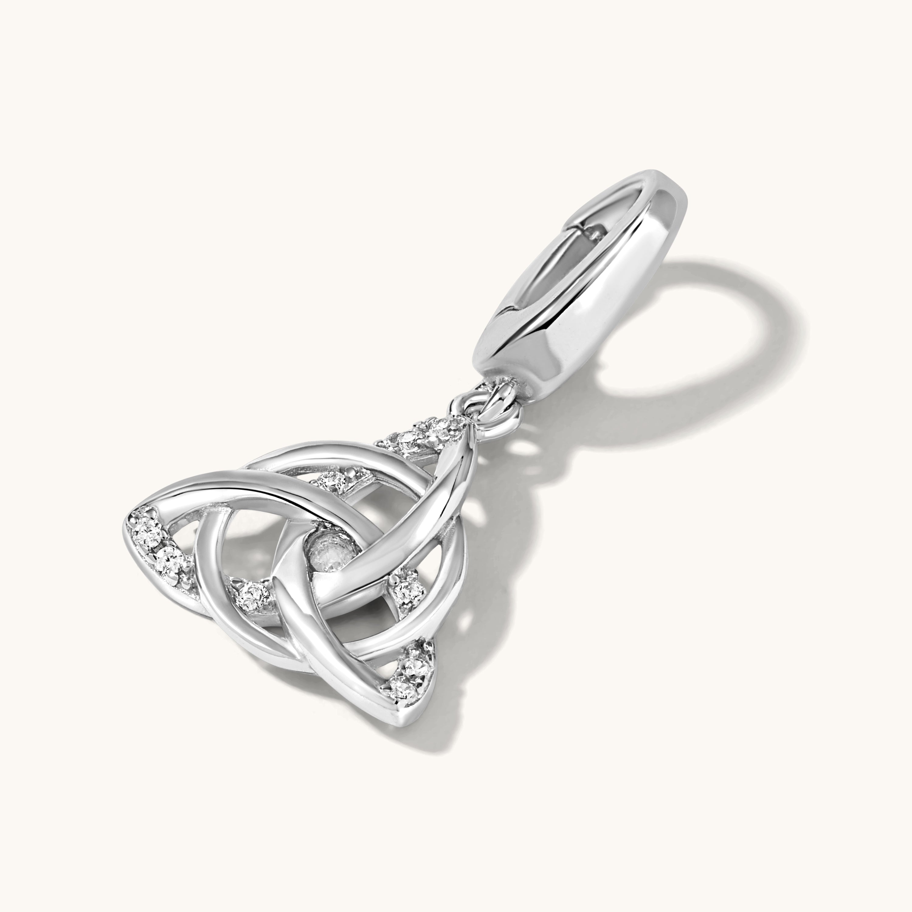 Stone studded Silver Triquetra symbol charm lying on a light cream background with shadow