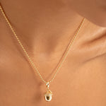 A close-up of a delicate gold chain necklace with an acorn pendant, worn on a model's neck.