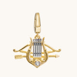 A gold lyre and arrow pendant charm with a clear round gemstone at the base, shown on a plain off-white background.