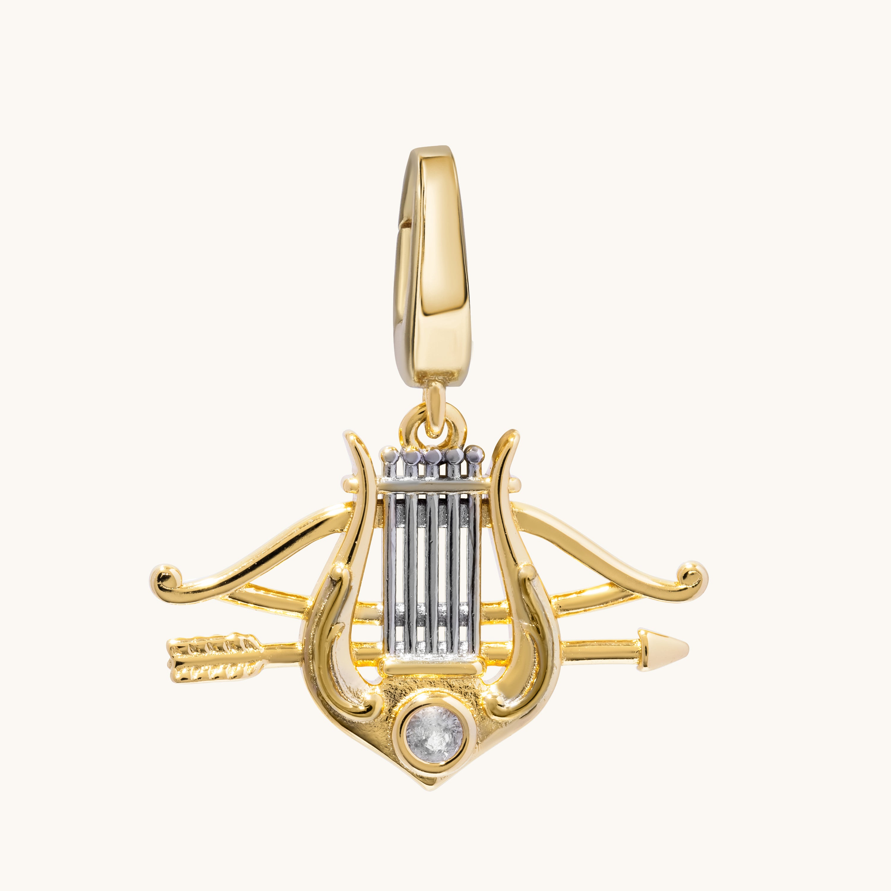 A gold lyre and arrow pendant charm with a clear round gemstone at the base, shown on a plain off-white background.