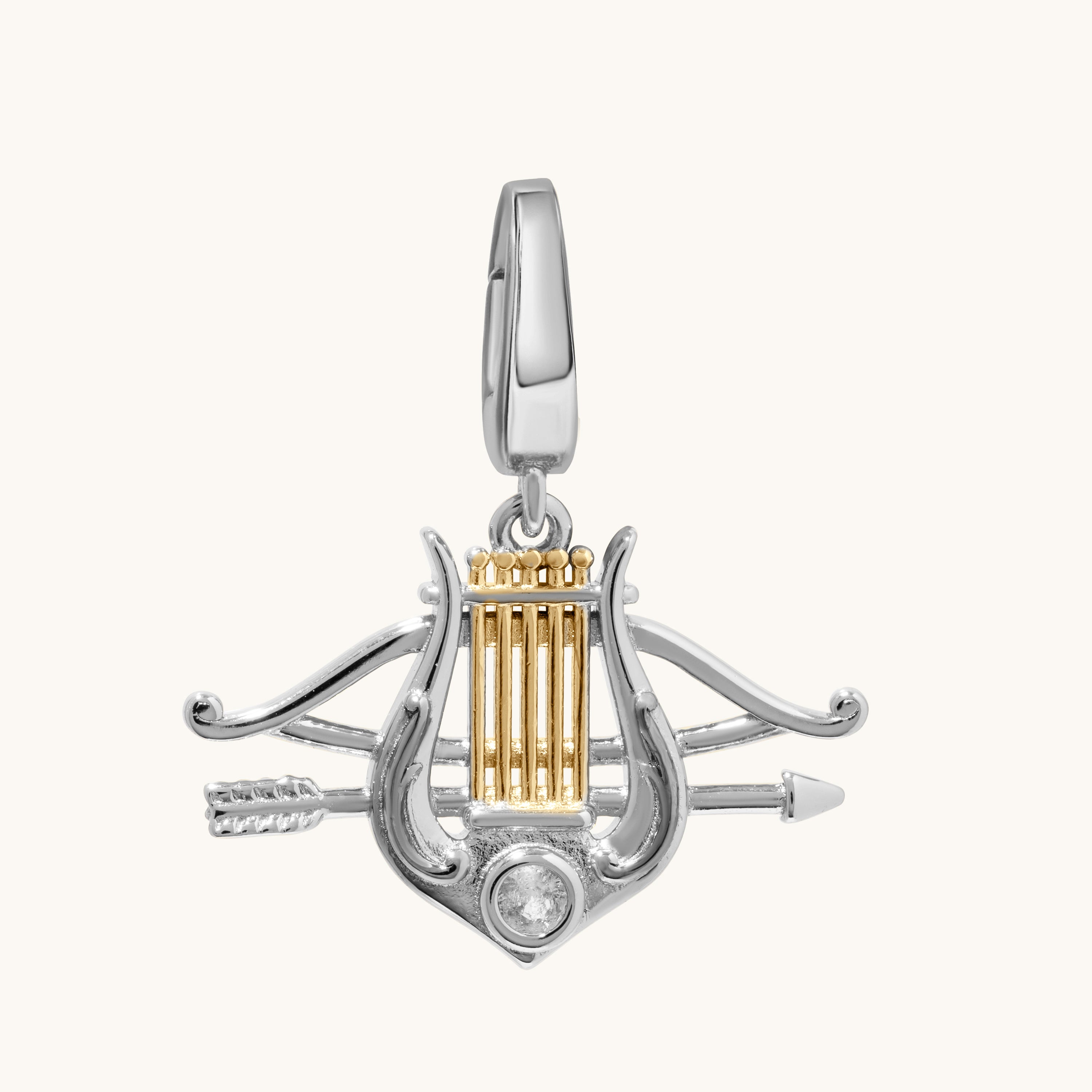 A two-tone silver and gold charm pendant depicting a lyre with crossed arrows and a clear round gemstone, shown on a light cream background.
