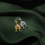 Two small house-shaped charms, one gold-toned and one silver-toned, displayed on draped dark green fabric.