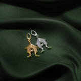 Two small house-shaped charms, one gold-toned and one silver-toned, displayed on draped dark green fabric.