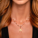 A woman wearing a gold pendant necklace with round beads, featuring a geometric design, and a black V-neck top.