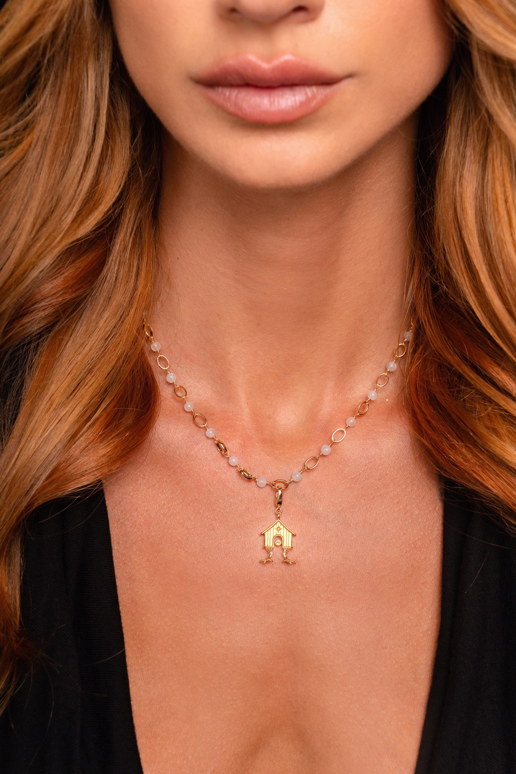 A woman wearing a gold pendant necklace with round beads, featuring a geometric design, and a black V-neck top.