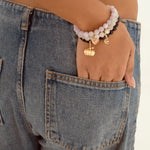 A close-up of a person wearing beaded bracelets with gold charms on their wrist, paired with blue denim jeans.