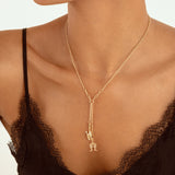 A close-up of a model wearing a delicate gold chain necklace with a double-layered design and a small dangling charm, styled with a black lace camisole top.