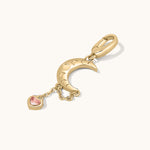 Gold charm with moon and heart-shaped gem on a white background