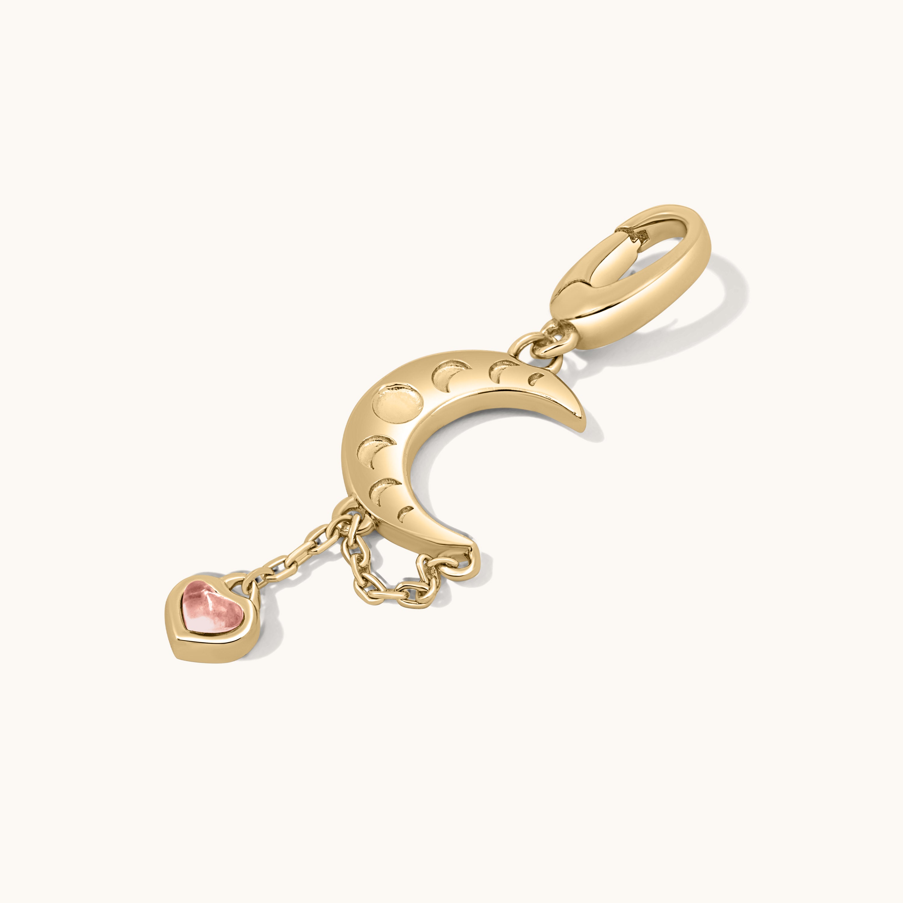 Gold charm with moon and heart-shaped gem on a white background