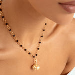 A close-up of a model wearing a delicate gold chain necklace with alternating black  beads and gold chain links and a small gold pumpkin pendant.