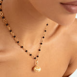 A close-up of a model wearing a delicate gold chain necklace with alternating black  beads and gold chain links and a small gold pumpkin pendant.
