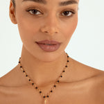 A close-up of a woman wearing a delicate gold necklace with small black beads and a gold pumpkin-shaped pendant, set against a clean white background.