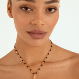 A close-up of a woman wearing a delicate gold necklace with small black beads and a gold pumpkin-shaped pendant, set against a clean white background.
