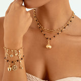 A close-up of a model wearing a layered gold necklace with a small pumpkin pendant and a matching gold charm bracelet with celestial charms.