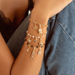 A close-up of a person wearing a stack of three delicate charm bracelets on their wrist, paired with a black lace camisole and blue denim shorts.