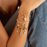 A close-up of a person wearing a stack of three delicate charm bracelets on their wrist, paired with a black lace camisole and blue denim shorts.