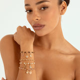 A close-up of a woman wearing multiple delicate charm bracelets on her left wrist, including crescent moons, stars, and hearts in rose gold and silver tones, against a clean white background.