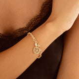 A close-up of a delicate gold chain bracelet with a small circular Pentacle  charm, worn on a woman's wrist.