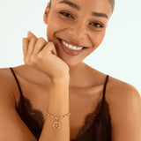 A smiling woman with her hair pulled back wears a delicate gold chain bracelet with a Pentacle sign charm, paired with a black lace camisole top against a clean white background.