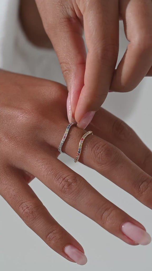 Woman putting on colored gemstone ring set in gold and silver.